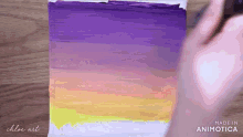a person is painting a purple and yellow sunset on a canvas .