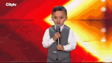 a young boy in a suit and tie is holding a microphone on a city tv screen