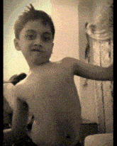 a young boy without a shirt is sitting on a bed