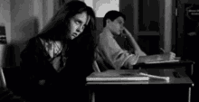 a man and a woman are sitting at a desk in a classroom .