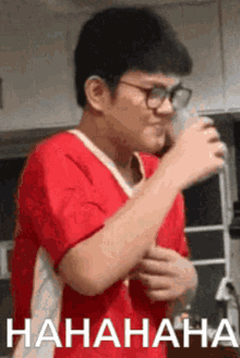 a man wearing glasses and a red shirt is laughing while holding a glass of water .