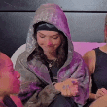 a woman wearing a purple jacket with a hood is sitting next to another woman .