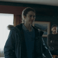 a woman wearing a jacket with a fur hood stands in a dark room