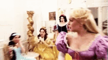 a group of women dressed as princesses are standing in a room . one of the women is wearing a purple dress .