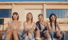 a group of young women wearing sunglasses are sitting on a bed in front of a building