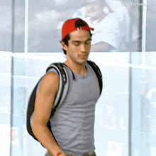a man wearing a red baseball cap and a grey tank top is walking
