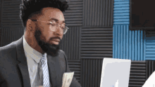 a man in a suit and tie is sitting in front of a laptop and holding a bunch of money