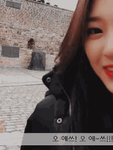 a woman in a black jacket is smiling with a brick wall in the background
