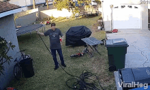 a man is holding a red cup and a hose in a backyard with a trampoline and trash cans ..