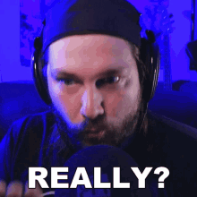 a man with a beard wearing headphones says really in front of a microphone