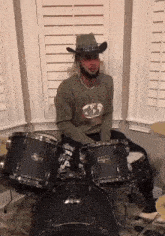 a man wearing a cowboy hat is playing a set of drums