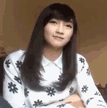 a woman with long hair is wearing a white sweater with black flowers on it and making a funny face .