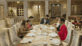 a group of people are sitting at a long dining table eating food .