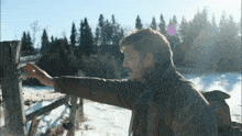 a man reaches out to touch a wooden fence post in a snowy field