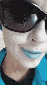 a woman wearing sunglasses and blue lipstick smiles for the camera