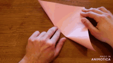 a person folding a piece of pink paper with the words made in animotica visible