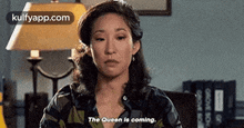a woman is sitting in front of a lamp and talking about the queen coming .