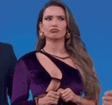 a woman in a purple dress with a plunging neckline is making a funny face .