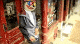 a man with a clown face on his head standing in front of a red door
