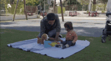 a man is playing with a baby on a blanket in a park with the letter a in the background