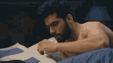 a shirtless man with a beard is laying on a bed with his head on a pillow .