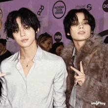 a man in a fur coat stands next to another man in a white shirt on a red carpet
