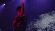 a person giving a peace sign in front of a purple background with the letter d on it