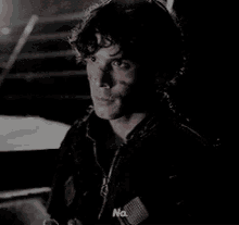 a man in a black jacket is sitting in a dark room and talking to someone .