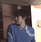 a man wearing a blue sweater and a necklace is standing in a room .