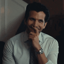 a man in a striped shirt and tie is smiling and holding his hand to his chin