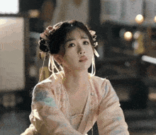 a woman in a pink dress with flowers in her hair is sitting on the floor and looking at the camera .