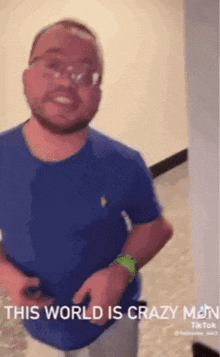 a man wearing glasses and a blue shirt is standing in front of a white wall .