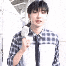 a young man in a plaid shirt and tie is holding a fan in his hand .