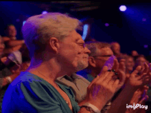 a woman in a blue shirt is clapping her hands in a crowd of people