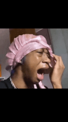 a man wearing a pink hat is yawning and covering his mouth with his hand .