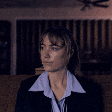 a woman in a suit and blue shirt is sitting on a couch looking at something .