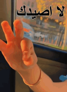 a hand is making a peace sign in front of a window with arabic writing