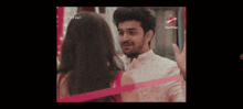 a man and a woman are standing next to each other and looking at each other with a pink ribbon wrapped around them .