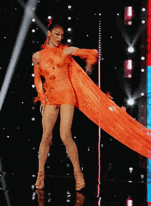 a drag queen in a long orange dress is dancing on a stage