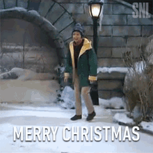 a man in a green jacket is walking in the snow with the words merry christmas behind him