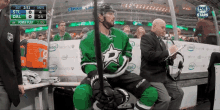 a hockey player in a green jersey sits on the bench during a game sponsored by intel