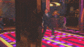 a man in a suit is dancing on a purple and yellow dance floor
