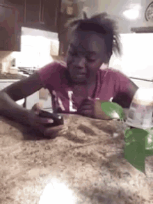a girl in a pink shirt is sitting at a table looking at her phone .