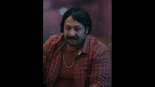 a man with a mustache and a red shirt is sitting on a couch .