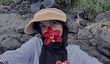 a woman wearing a hat and sunglasses has a flower in her mouth