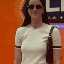 a woman wearing sunglasses and a white shirt is standing in front of a sign .