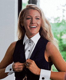 a woman wearing a white shirt and a black vest smiles