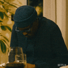 a man wearing a blue beanie and glasses sits at a table with a netflix logo on the bottom