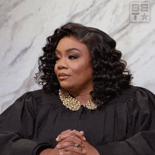 a woman with curly hair is wearing a black gown with gold collar