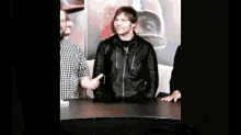a man in a black leather jacket is standing in front of a football helmet